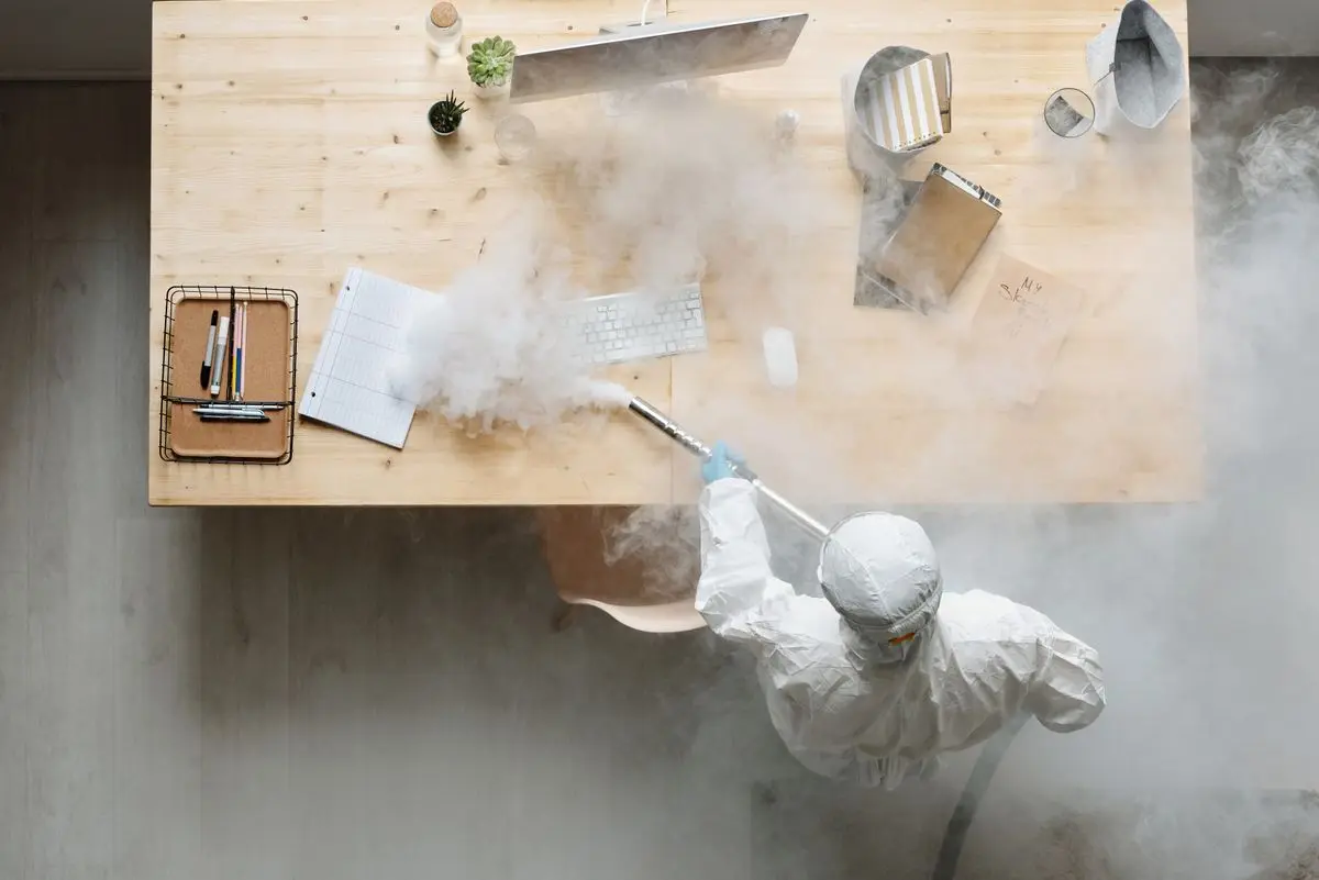 A technician in a white suit fogging a surface.