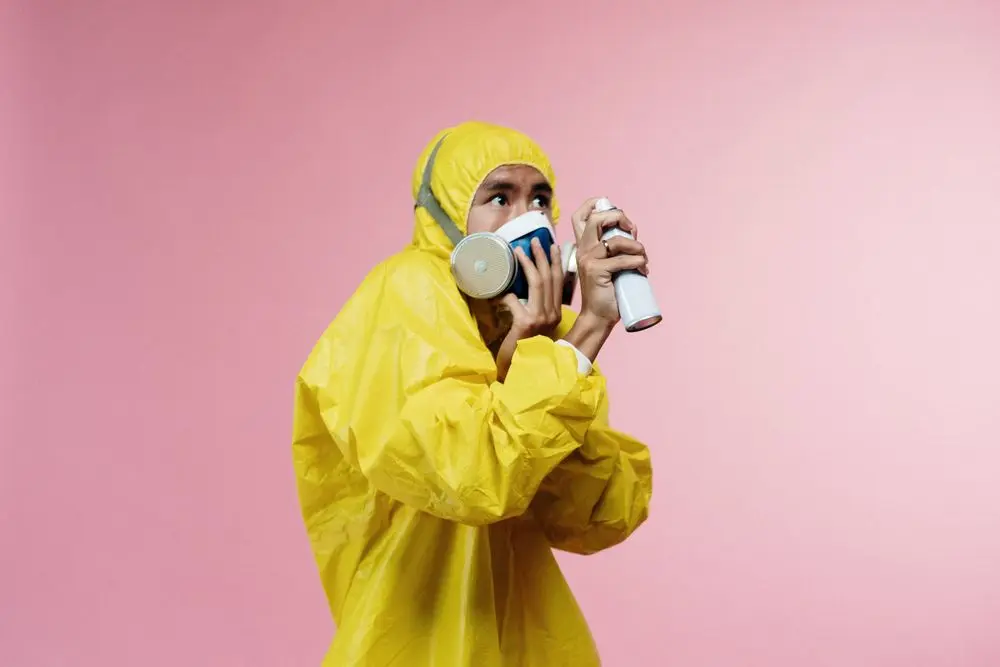 A technician in a yellow suit and respirator holding a spray.