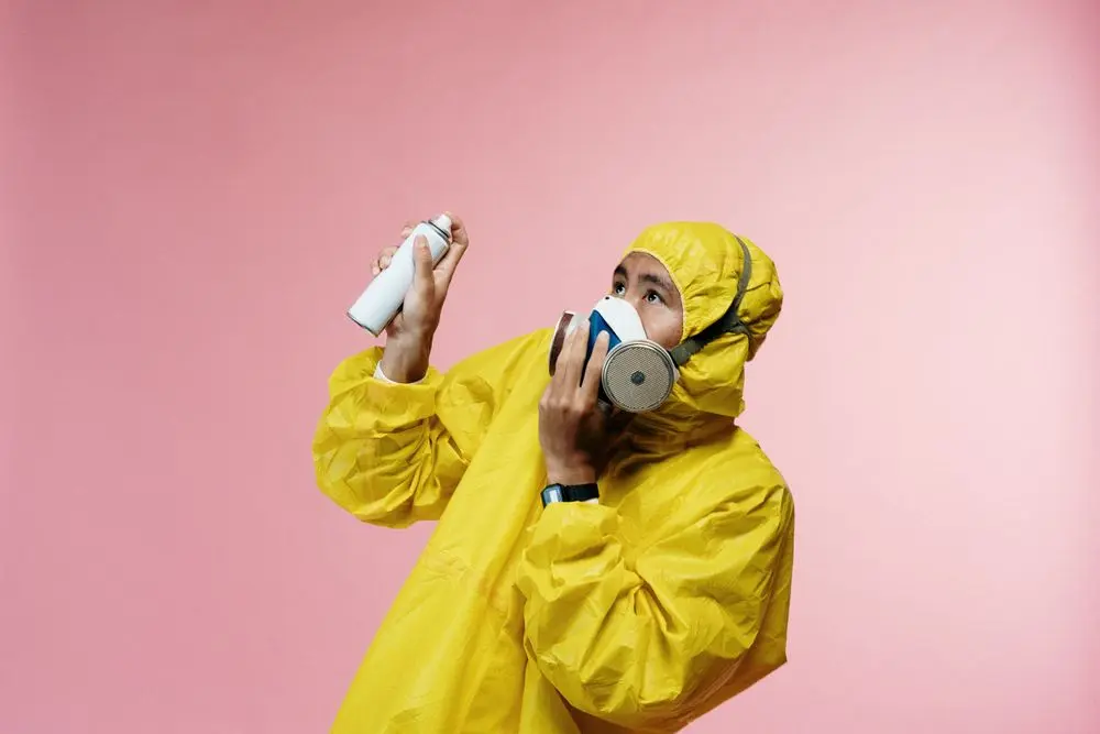 A technician in a yellow suit and respirator using a spray.